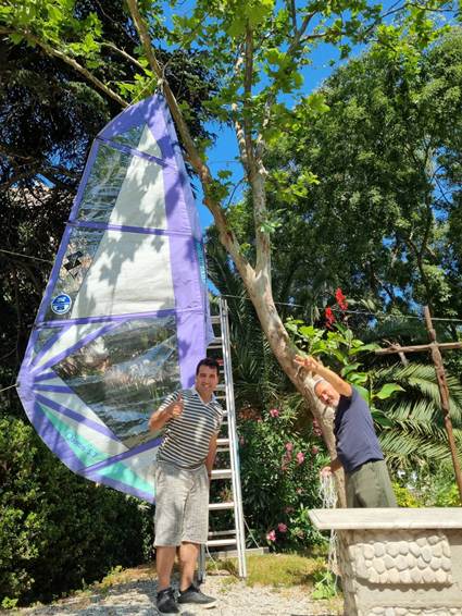 The image shows two people, one holding a large, colorful kite with a reflective surface, under a tree with green leaves, and a stone path in the background.

AI-generated content may be incorrect.