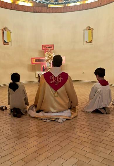 A group of children in traditional robes are seated in a church, each holding a small object, around a ceremonial golden chair.

AI-generated content may be incorrect.