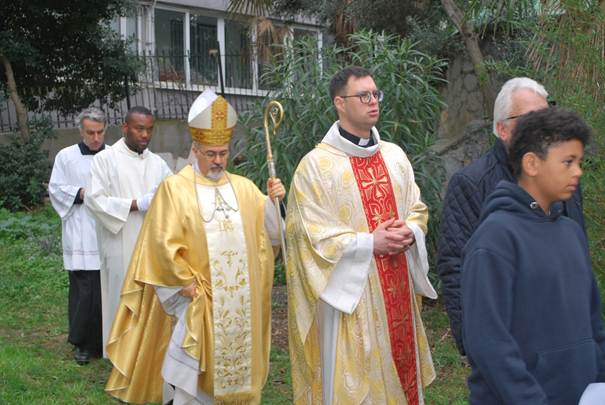 The image shows a group of people dressed in religious attire, including a priest, wearing elaborate robes and hoods, standing outdoors among trees and foliage.

AI-generated content may be incorrect.