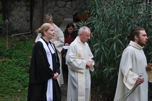 The image depicts a group of people, including a man in a white robe and a woman in a black dress, standing outdoors among greenery and stone.

AI-generated content may be incorrect.